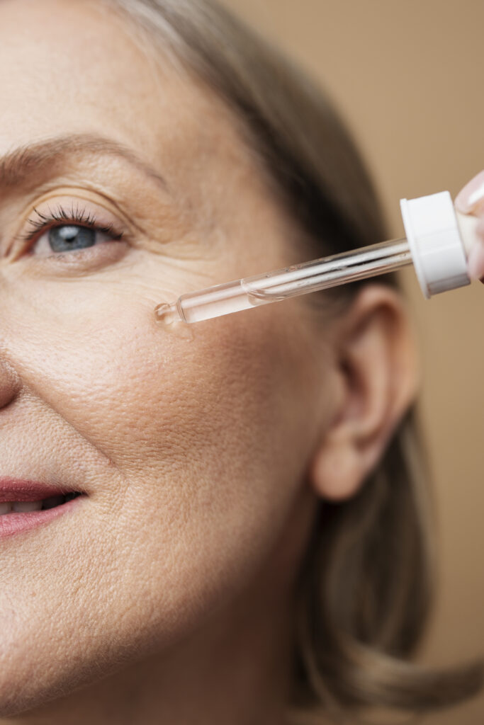 Na imagem, uma mulher madura passando sérum facial no rosto. O ácido azelaico é fundamental para uma rotina de skincare.
