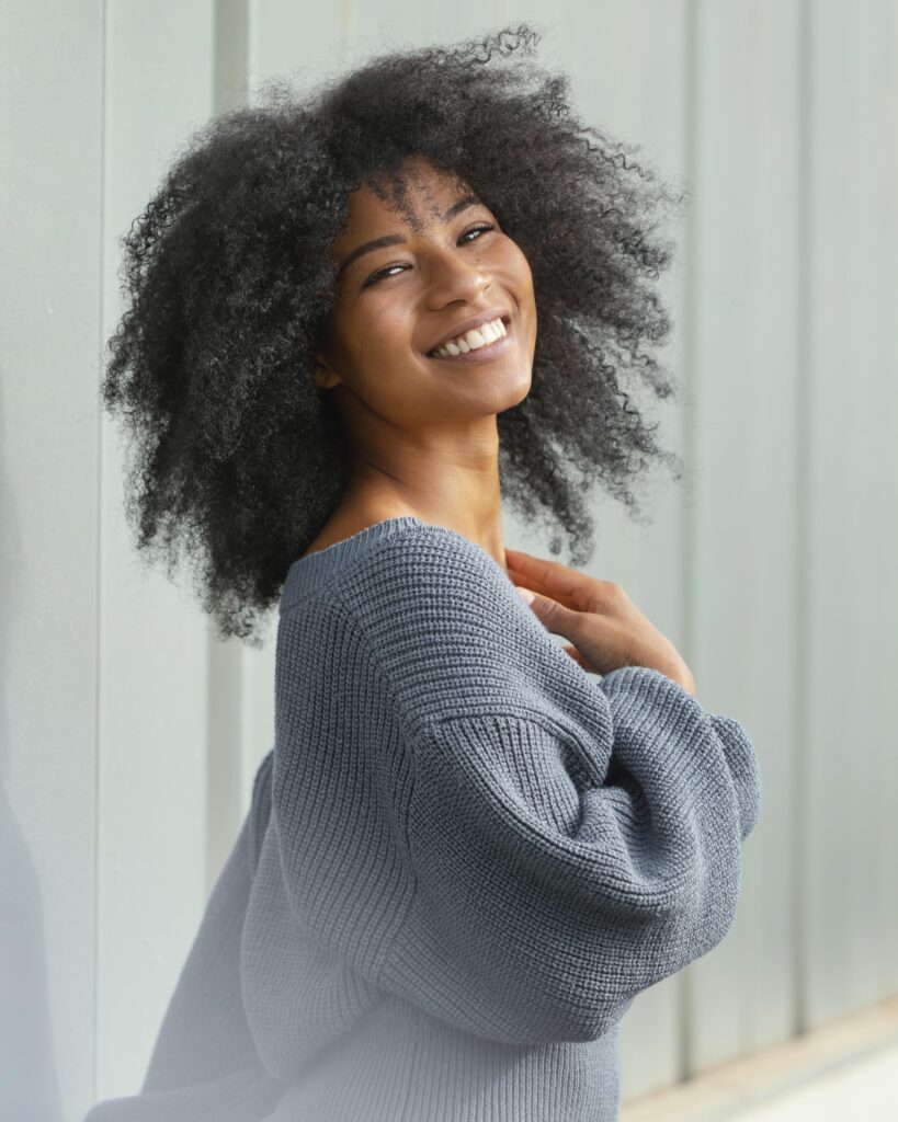 Uma mulher com pele negra sorrindo, exaltando beleza.